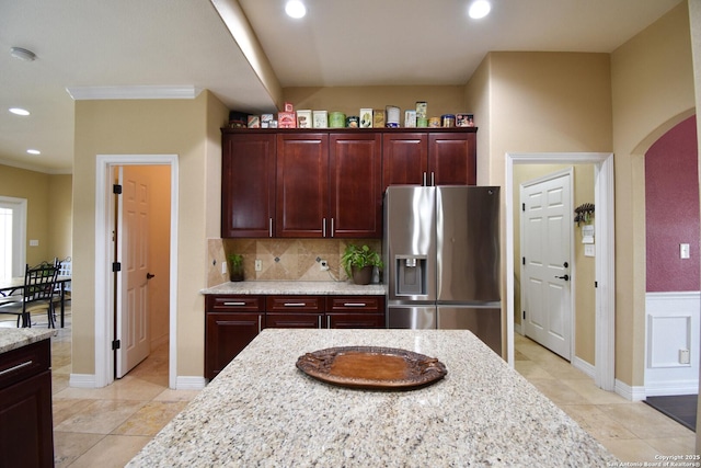 kitchen featuring arched walkways, decorative backsplash, stainless steel fridge with ice dispenser, light stone counters, and recessed lighting