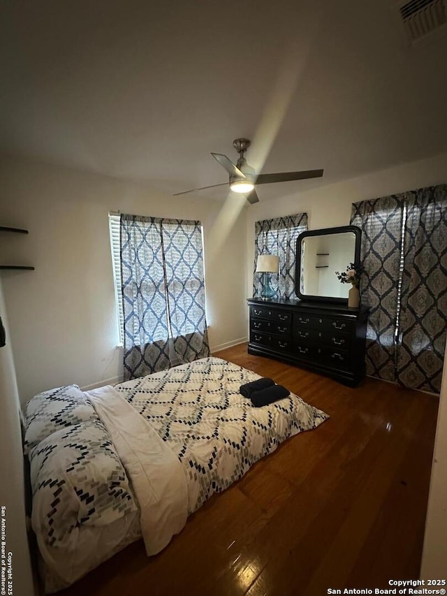 bedroom with dark wood-style floors, ceiling fan, visible vents, and baseboards