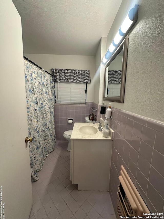 bathroom with radiator, tile patterned flooring, a textured ceiling, vanity, and tile walls