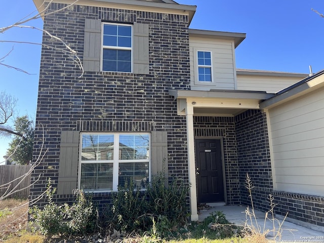 view of exterior entry with brick siding and fence