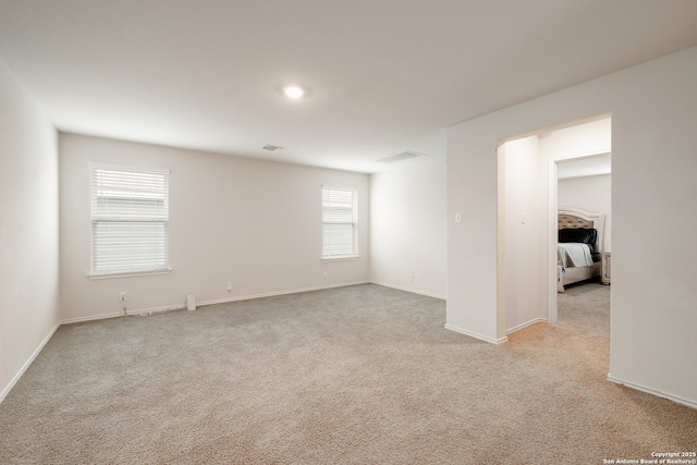 empty room with light carpet, visible vents, and baseboards