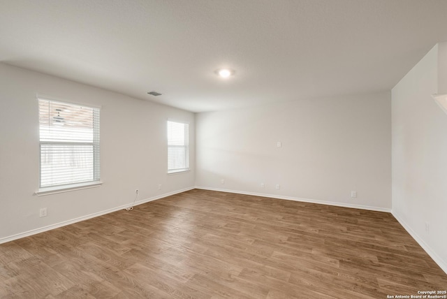 spare room featuring light wood-type flooring, visible vents, and baseboards