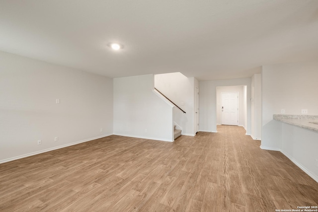 unfurnished living room with stairs, light wood-type flooring, and baseboards