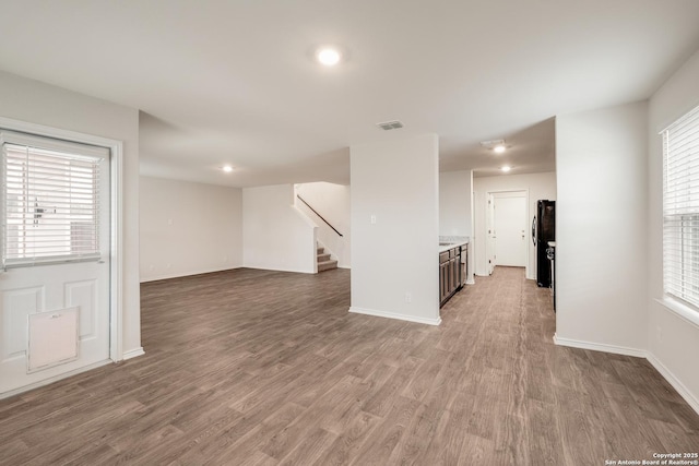 unfurnished living room featuring baseboards, stairs, visible vents, and wood finished floors