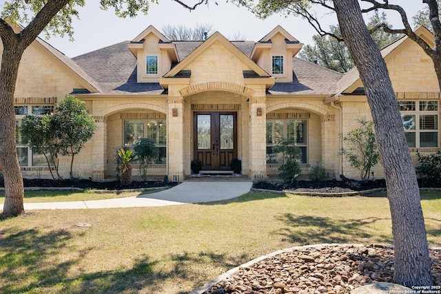 view of front facade with stone siding, french doors, a shingled roof, and a front yard