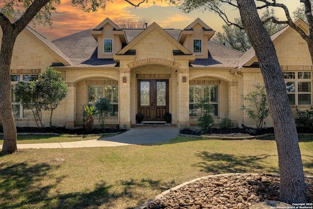 view of front of house featuring a front lawn, french doors, stone siding, and roof with shingles