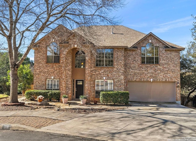 traditional-style home featuring a garage, driveway, brick siding, and roof with shingles