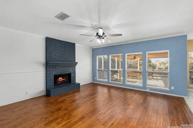 unfurnished living room with a fireplace, wood finished floors, visible vents, a ceiling fan, and crown molding