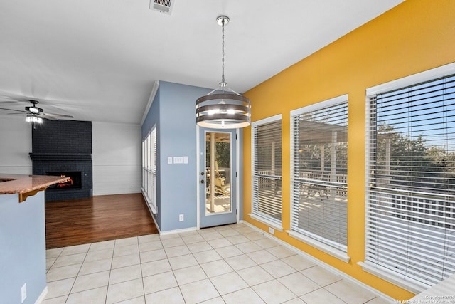 unfurnished dining area with light tile patterned floors, ceiling fan with notable chandelier, a fireplace, visible vents, and vaulted ceiling