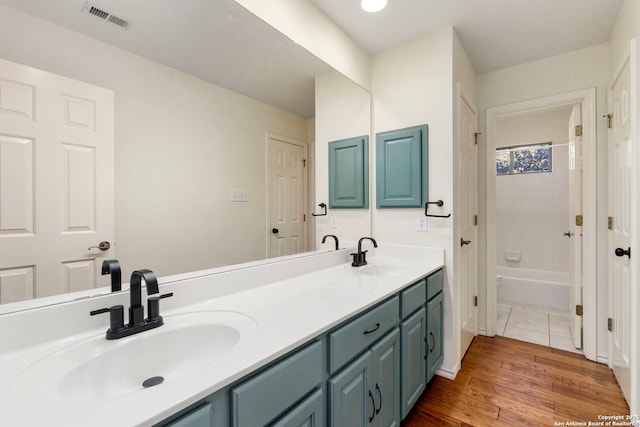 full bath with double vanity, visible vents, a sink, and wood finished floors