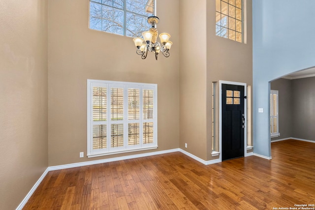 entryway with arched walkways, a notable chandelier, wood finished floors, a towering ceiling, and baseboards