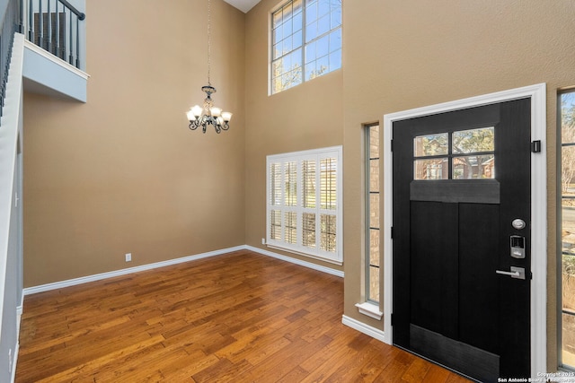 foyer entrance featuring an inviting chandelier, a towering ceiling, baseboards, and wood finished floors