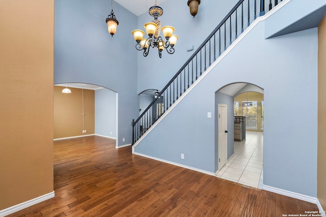 interior space featuring light wood finished floors, baseboards, arched walkways, a towering ceiling, and an inviting chandelier