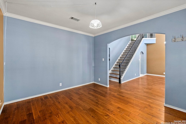 empty room with arched walkways, wood finished floors, visible vents, baseboards, and ornamental molding