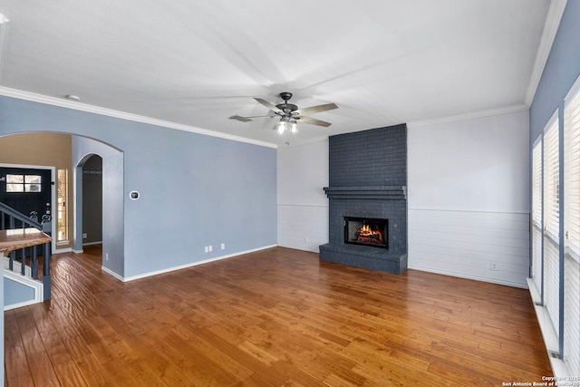 unfurnished living room with arched walkways, ornamental molding, a brick fireplace, and wood finished floors