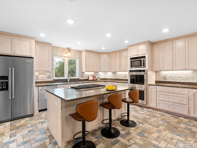 kitchen with tasteful backsplash, appliances with stainless steel finishes, a breakfast bar, light brown cabinetry, and a sink