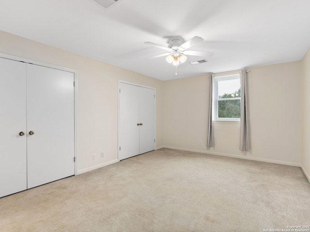 unfurnished bedroom featuring visible vents, light carpet, baseboards, and two closets