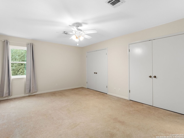 unfurnished bedroom featuring light carpet, baseboards, visible vents, and two closets