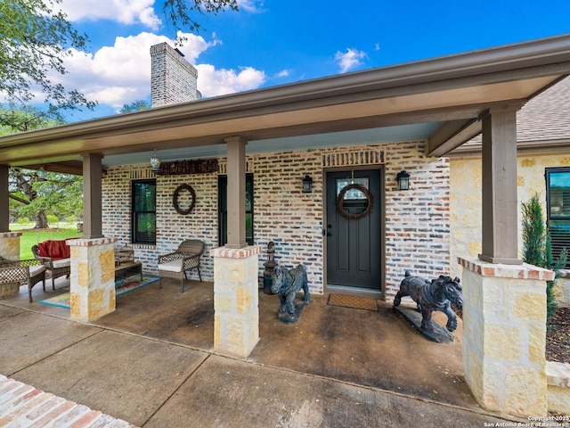 entrance to property with covered porch, brick siding, and a chimney