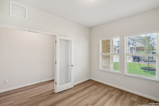 unfurnished room featuring light wood finished floors, visible vents, and a healthy amount of sunlight