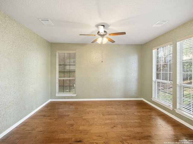 empty room featuring a textured wall, wood finished floors, visible vents, and baseboards