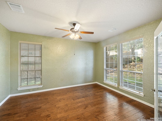 spare room featuring a textured wall, dark wood finished floors, visible vents, and baseboards