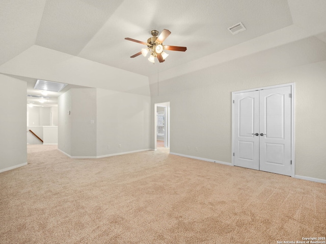 empty room featuring a tray ceiling, light colored carpet, visible vents, ceiling fan, and baseboards