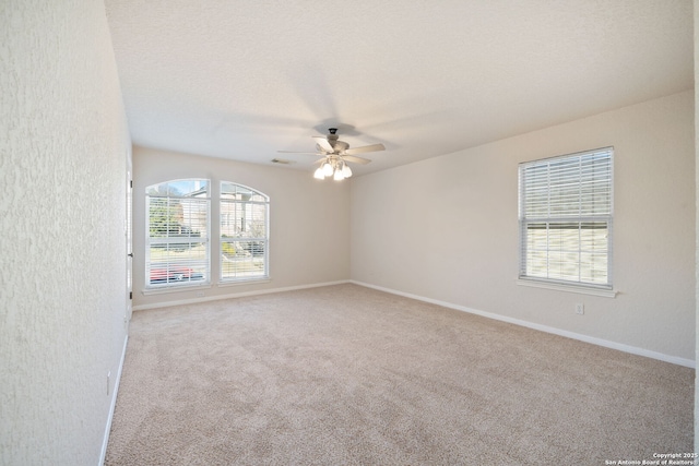 unfurnished room with a textured ceiling, light colored carpet, visible vents, baseboards, and a ceiling fan