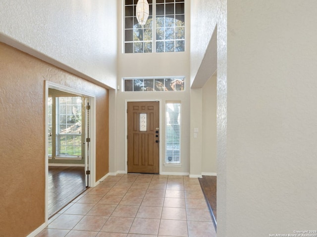 foyer entrance featuring a textured wall, light tile patterned flooring, and baseboards