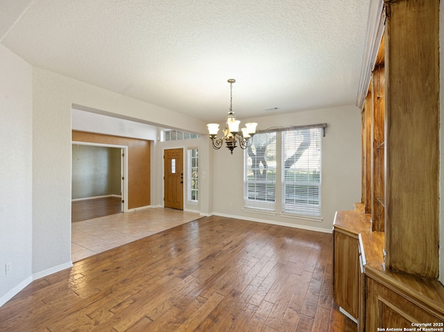 unfurnished dining area with light wood finished floors, baseboards, a chandelier, and a textured ceiling