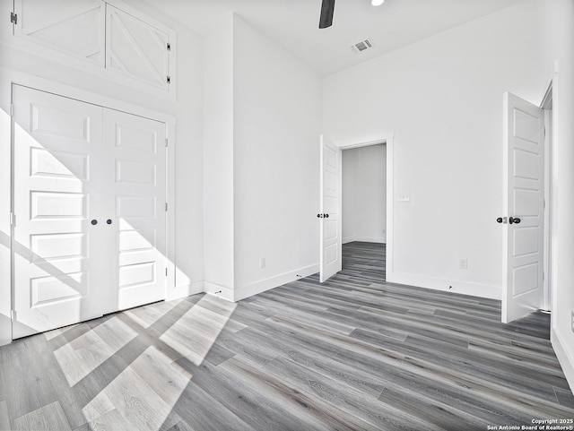 unfurnished bedroom featuring visible vents, a high ceiling, a ceiling fan, wood finished floors, and baseboards
