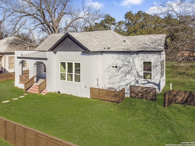 rear view of house featuring a shingled roof, fence, a lawn, and stucco siding