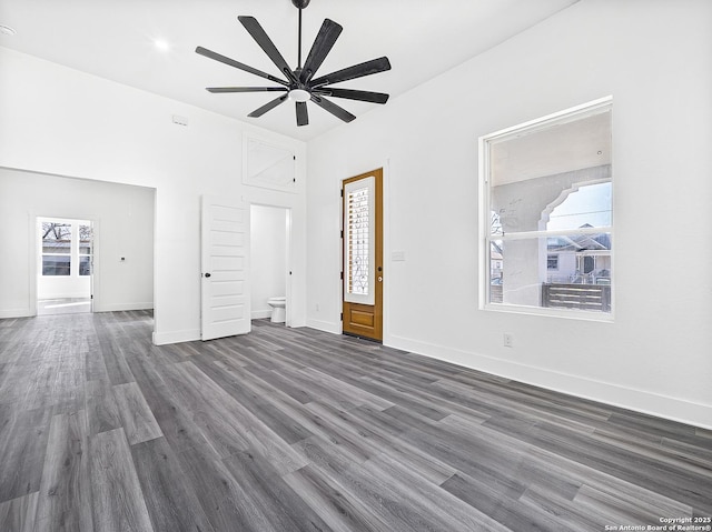 unfurnished room featuring dark wood-style floors, a towering ceiling, a ceiling fan, and baseboards