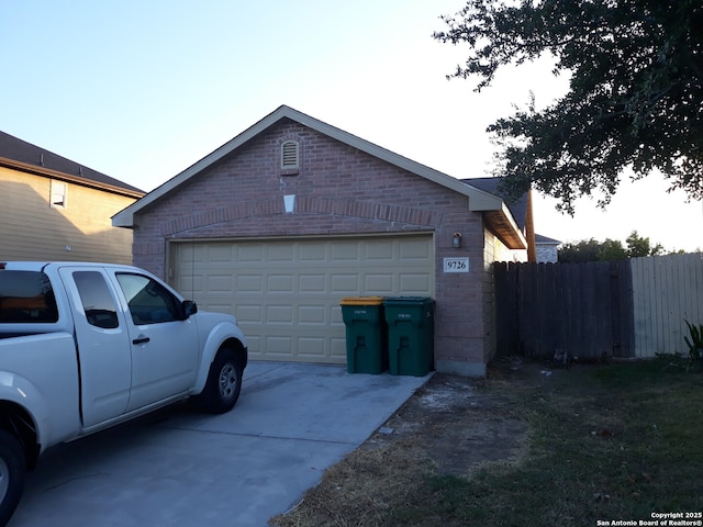 view of side of property with a garage, driveway, brick siding, and fence