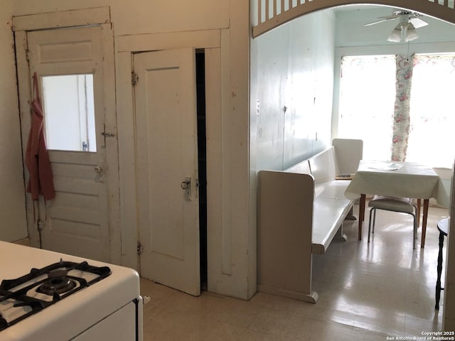 kitchen with arched walkways, white range with gas stovetop, a ceiling fan, light countertops, and light floors