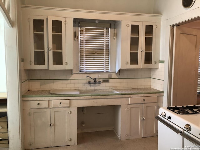 kitchen featuring glass insert cabinets, light countertops, gas range gas stove, and decorative backsplash