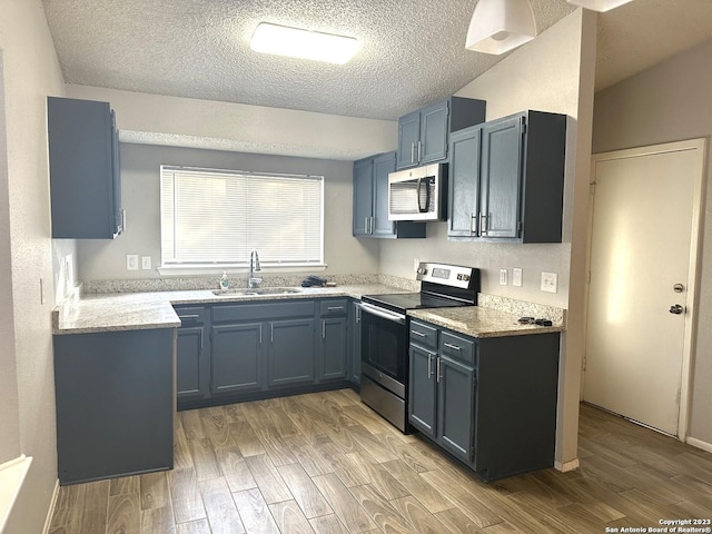 kitchen featuring a textured ceiling, stainless steel appliances, light wood-type flooring, and a sink