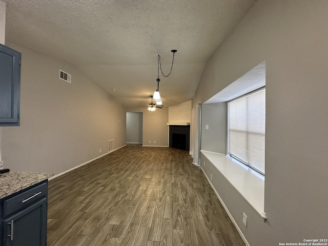 unfurnished living room featuring dark wood-style flooring, a fireplace, visible vents, vaulted ceiling, and ceiling fan