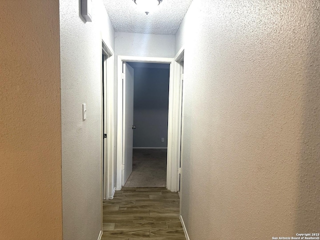 hallway featuring a textured ceiling, a textured wall, and wood finished floors