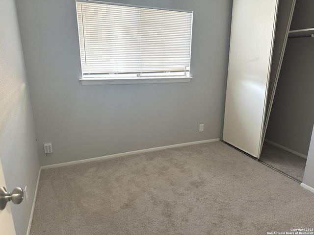 unfurnished bedroom featuring baseboards, a closet, and light colored carpet