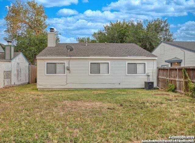 rear view of house with central air condition unit, a chimney, fence, and a yard