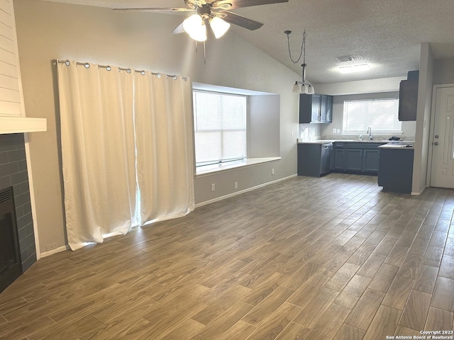 unfurnished living room with dark wood finished floors, a fireplace, lofted ceiling, ceiling fan, and a textured ceiling