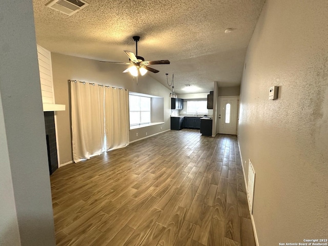 unfurnished living room with visible vents, a textured wall, ceiling fan, dark wood-style flooring, and a textured ceiling