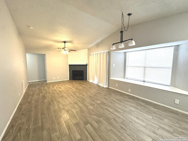 unfurnished living room featuring a fireplace, a ceiling fan, vaulted ceiling, a textured ceiling, and wood finished floors