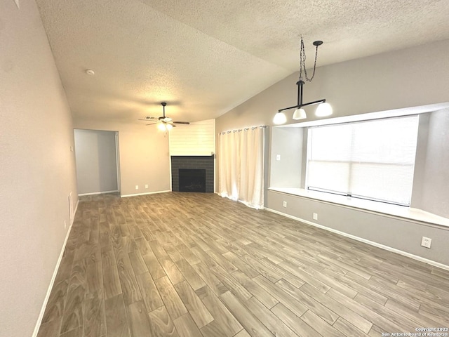 unfurnished living room with ceiling fan, a textured ceiling, a fireplace, wood finished floors, and vaulted ceiling