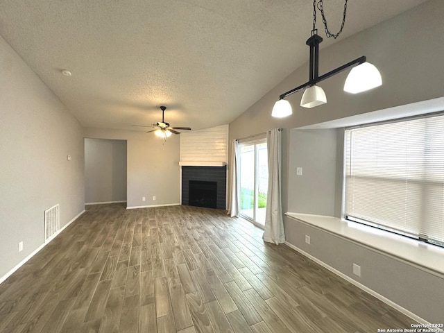 unfurnished living room featuring visible vents, dark wood finished floors, ceiling fan, a textured ceiling, and a brick fireplace