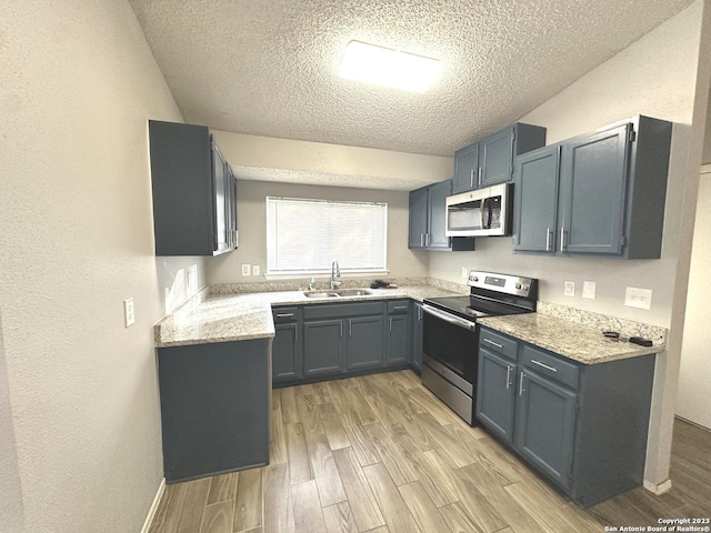 kitchen with baseboards, stainless steel appliances, a textured ceiling, wood finish floors, and a sink