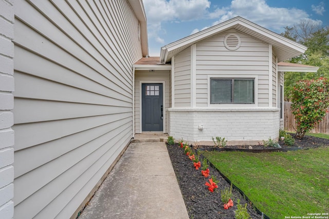 view of exterior entry featuring brick siding, a lawn, and fence