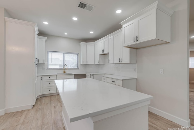 kitchen with visible vents, white cabinets, a kitchen island, a sink, and light wood-type flooring