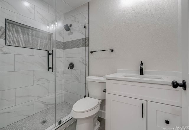 bathroom with toilet, a textured wall, a shower stall, and vanity